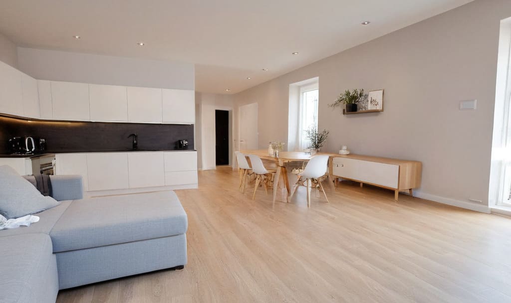 Nowoczesne, wykończone pod klucz wnętrze prezentujące jasny salon z aneksem kuchennym, przedstawione jako inspiracja dla osób poszukujących mieszkania na sprzedaż.